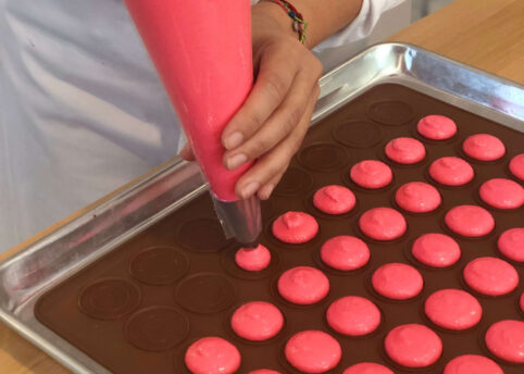 Pink Macaron batter being piped onto sheet tray