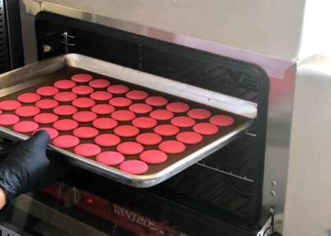 Pink macarons being taken out of oven